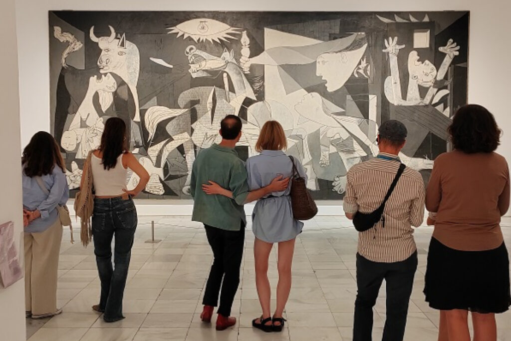 Egy férfi nézi Picasso Guernicáját egy galériában. A festmény monokróm és kaotikus. Egy nő ül a háttérben, nyugodt légkör. Spanyolban Otthon, Kása Heni Spanyolország, Madrid blog
