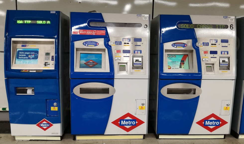 Három metrójegyautomata kék és fehér színben, képernyőkkel és feliratokkal. Mindegyik automata különböző szöveget jelenít meg.