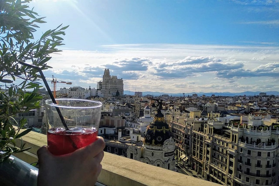 Madridi tetőterasz kilátással a Gran Vía pazar épületire, valaki egy poharat fog , amiben sangria van