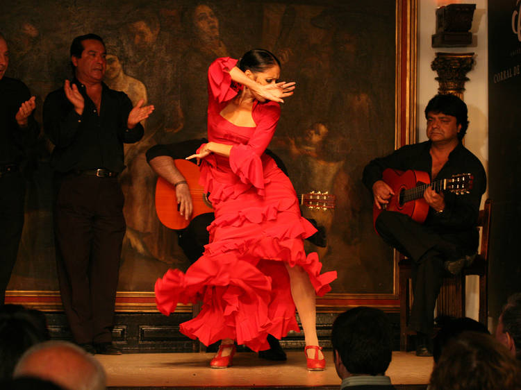 flamenco előadás Madridban, egy piros ruhás nő táncol, háttérben egy gitáros férfi ül, egy másik pedig áll és tapsol