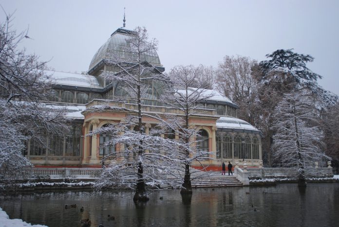 Madrid télen, a Retiro Parkban a Kristálypalota látható, hóval borított üvegház. Két ember sétál a havas tájon, tükröződő tó partján. Derűs, csendes hangulat.