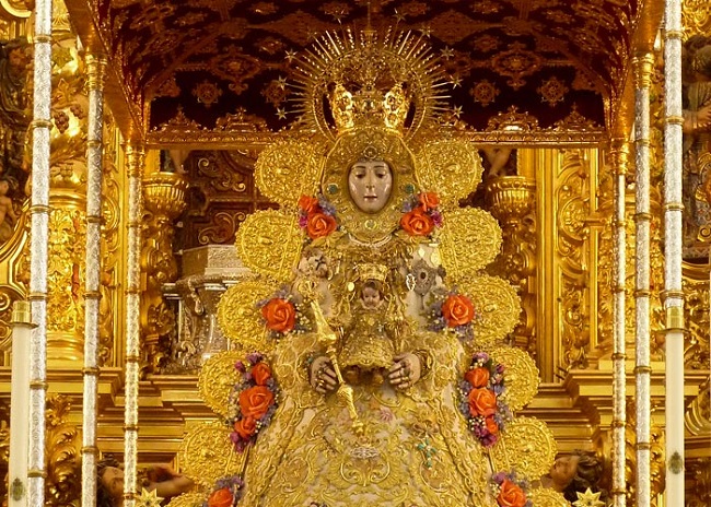 El Rocío, a gyógyítás madonnája. Aranyozott szobor koronával és díszekkel egy díszes háttér előtt. Színes rózsák és komplex minták fokozzák a kép pompáját.
