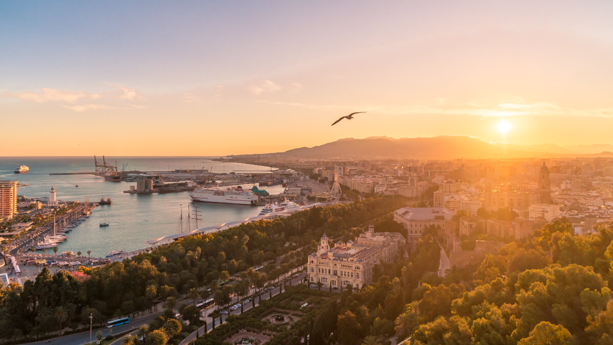 Panorámás kilátás Malaga kikötőjére (Muelle Uno) és a tengerparti sétányra naplementekor a Gibralfaro várból. Malaga látnivalók és 2026-os útikalauz a Spanyolban Otthon blogon.