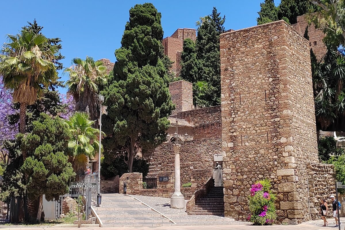 A malagai Alcazaba mór erődítményének tornya és pálmafák az utcáról fotózva. Malaga látnivalók és történelmi városnézés.