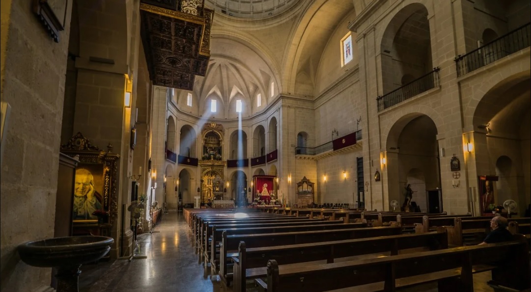 San Nicolás de Bari-társszékesegyház Alicante óvárosának szívében. A templom belső tere, padokkal, keresztelő medencével