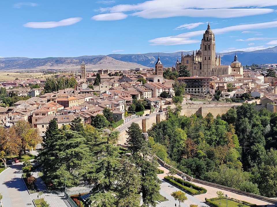 panoráma kép Segovia középkori városról, háttérben hegyek és kék ég felhőkkel