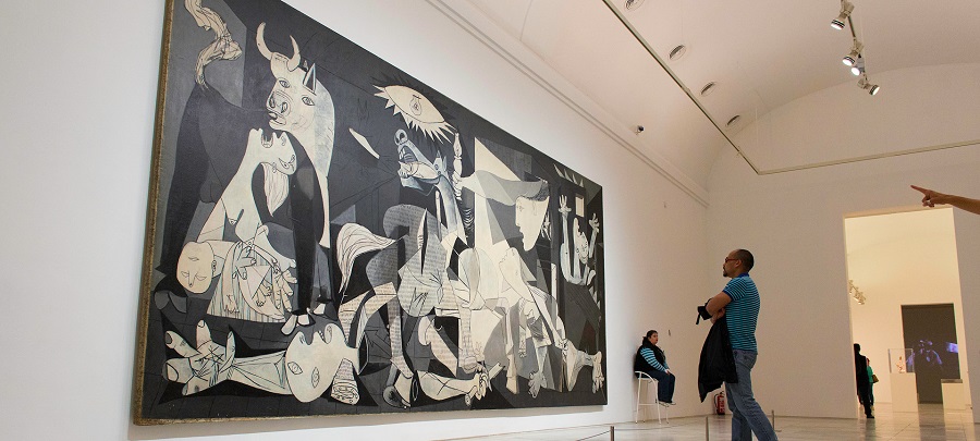 Múzeumban ember nézi Picasso Guernicáját. Nagy, fekete-fehér festmény káoszt ábrázolva. Fényes, tágas terem, nyugodt hangulat.