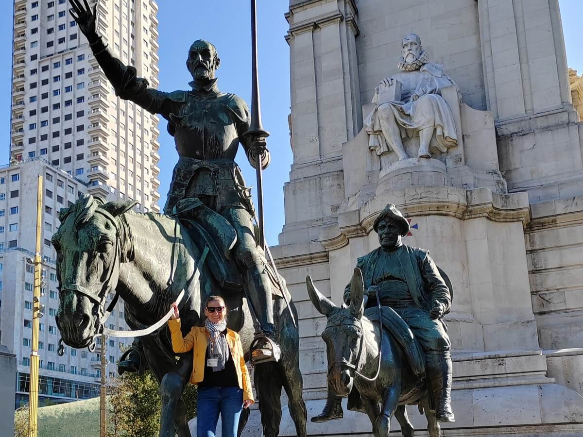 A madridi Plaza de España téren álló monumentális Cervantes-emlékmű Miguel de Cervantes író, valamint Don Quijote és Sancho Panza szobraival, és egy magyar idegenvezető sárga kabátban.