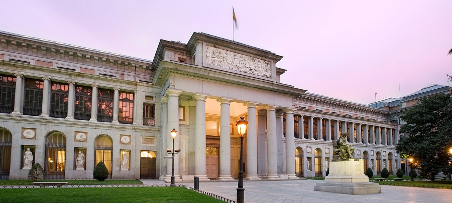A kép a madridi Prado Múzeum épületét ábrázolja rózsaszín égbolt alatt, klasszikus oszlopokkal és szobrokkal. Előtérben lámpa és szobor.