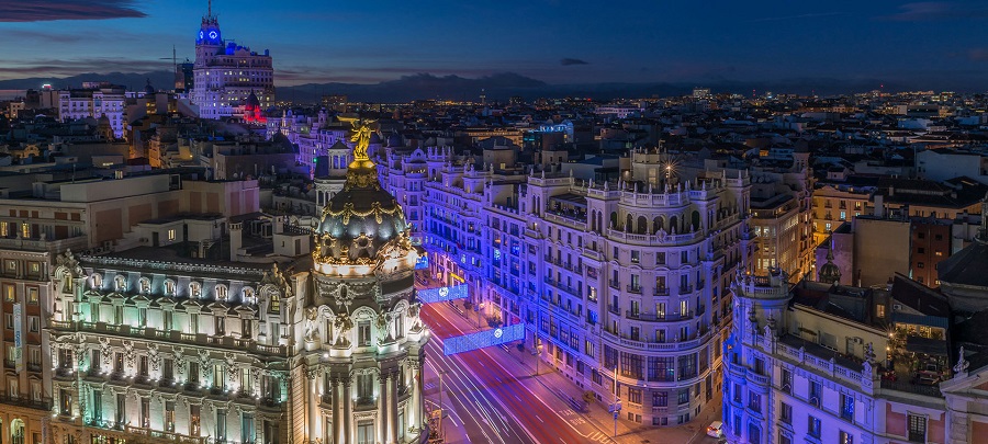 Éjszakai városi tájkép, a Gran Vía sugárút megvilágított klasszikus épületek Madridban. Az utca kék fénnyel kiemelve, a háttér sötétkék égbolt.