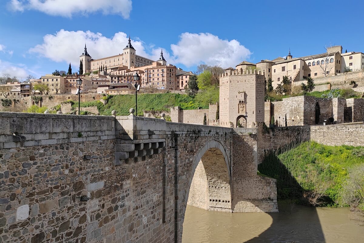 Kilátás a toledói Alcantara hídra (Puente de Alcántara) a Tajo folyó felett, a háttérben az Alcázar erőd monumentális tömbjével – Toledo látnivalók