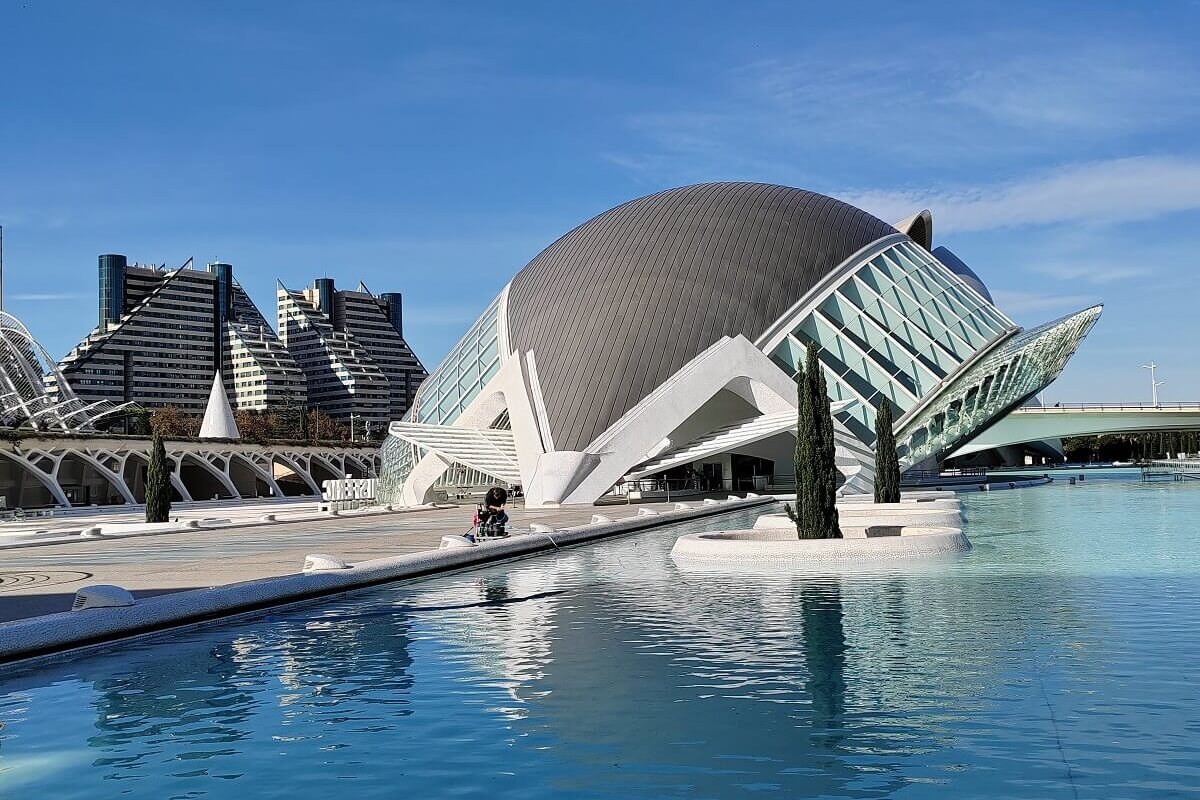 A valenciai Hemisfèric IMAX mozi szem alakú épülete és tükröződése a vízen, háttérben a Művészetek és Tudományok Városa modern felhőkarcolóival.