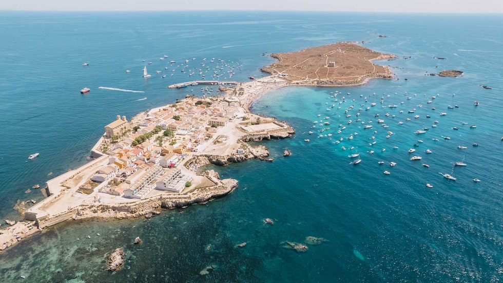 Légi felvétel Tabarca sziget (alicante) óvárossal, körülötte sok hajó a kék tengeren. Világos épületek és sziklás partvonal látható. Nyugodt hangulat.