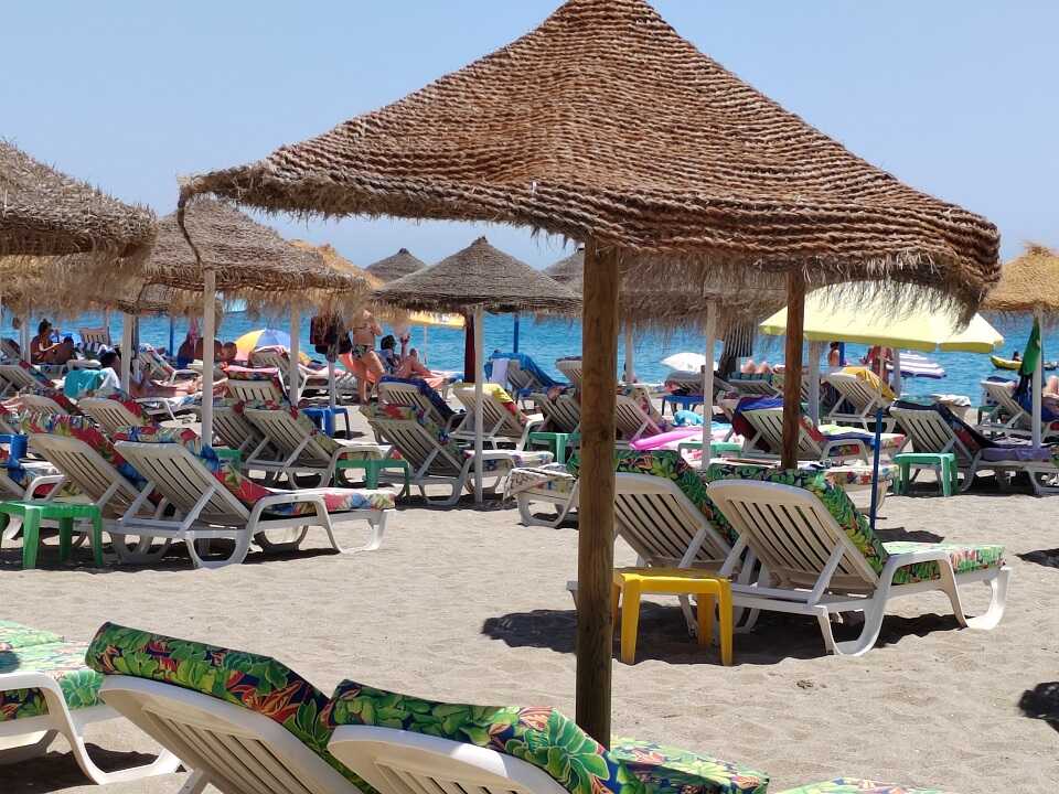 tengerpart napernyőkkel és napágyakkal rajtuk zöld matrac