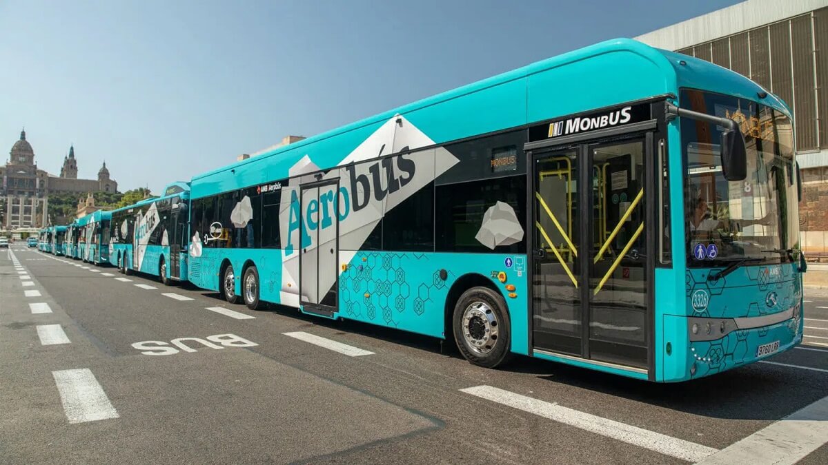 Kék színű repülőtéri Aerobúsok sorakoznak az út mentén Barcelona városában. Az autóbuszok oldalán felirat. A háttérben épületek láthatók.